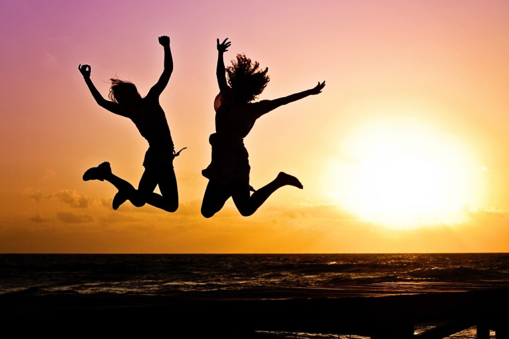 two girls jumping for joy on the beach at sunset